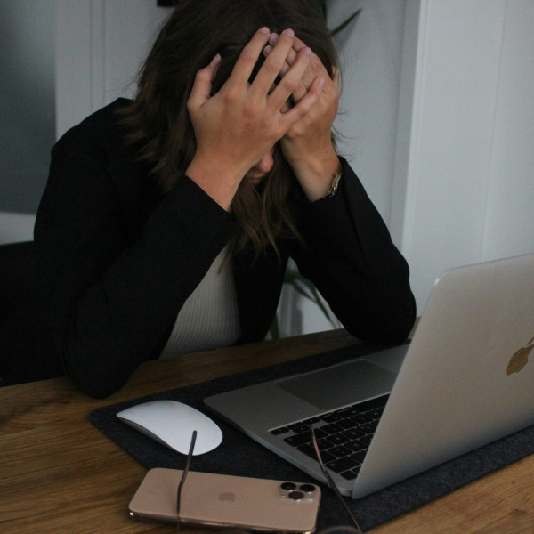 eine-frau-die-ihr-gesicht-bedeckt-wahrend-sie-auf-einen-laptop-schaut