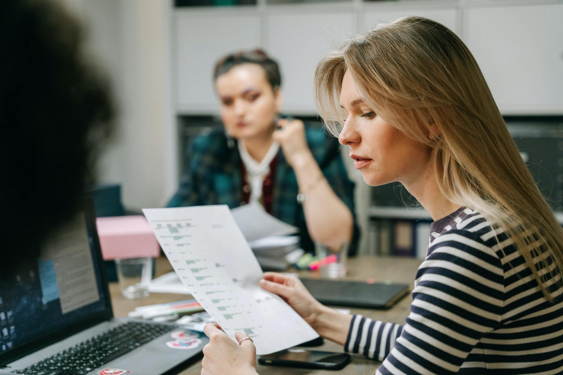 zwei-frauen-sitzen-an-einem-tisch-und-schauen-auf-ein-blatt-papier
