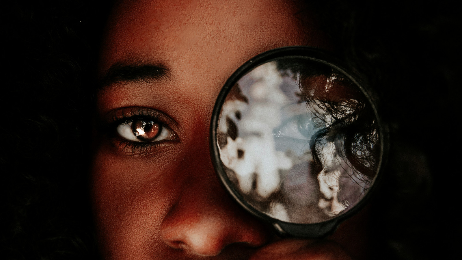 Eine Frau hält eine Lupe vor ihr Auge, auf der Suche nach passenden Inhalten