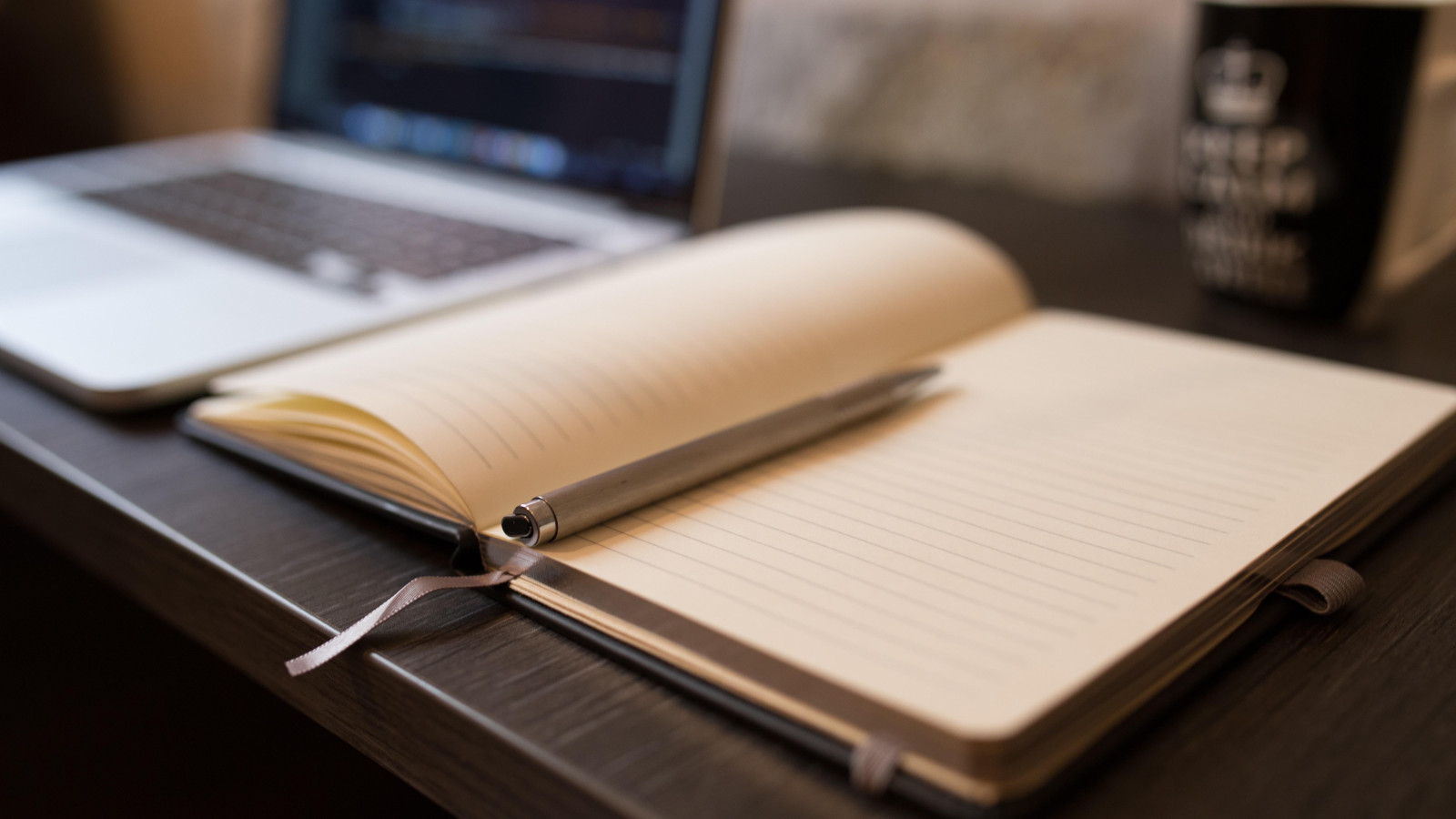 Laptop und aufgeklapptes Buch auf einem Schreibtisch