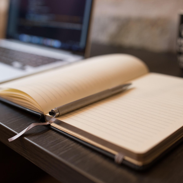 Laptop und aufgeklapptes Buch auf einem Schreibtisch