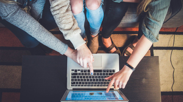 Drei Personen sitzen zusammen und zeigen auf einen Laptop-Bildschirm