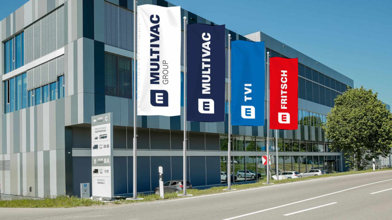 Das Bild zeigt das Logo "MULTIVAC" auf einer Fahne vor einem Gebäude